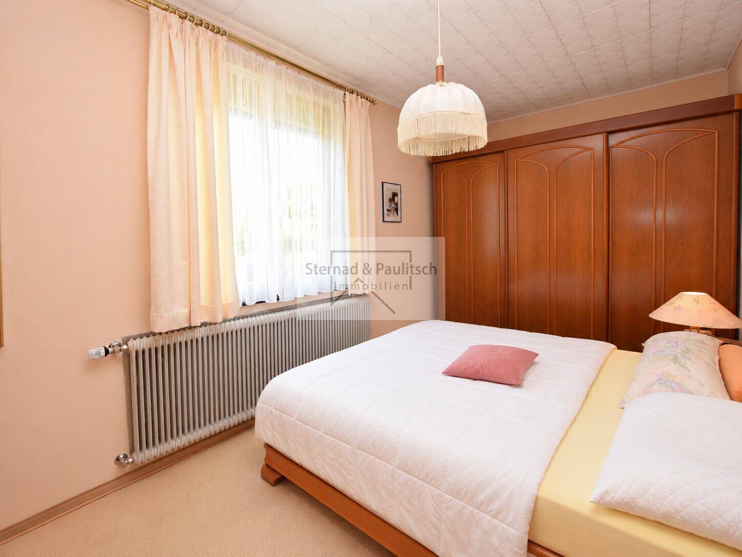 Schlafzimmer mit Doppelbett, großem Holzschrank und Fenster für natürliches Licht.