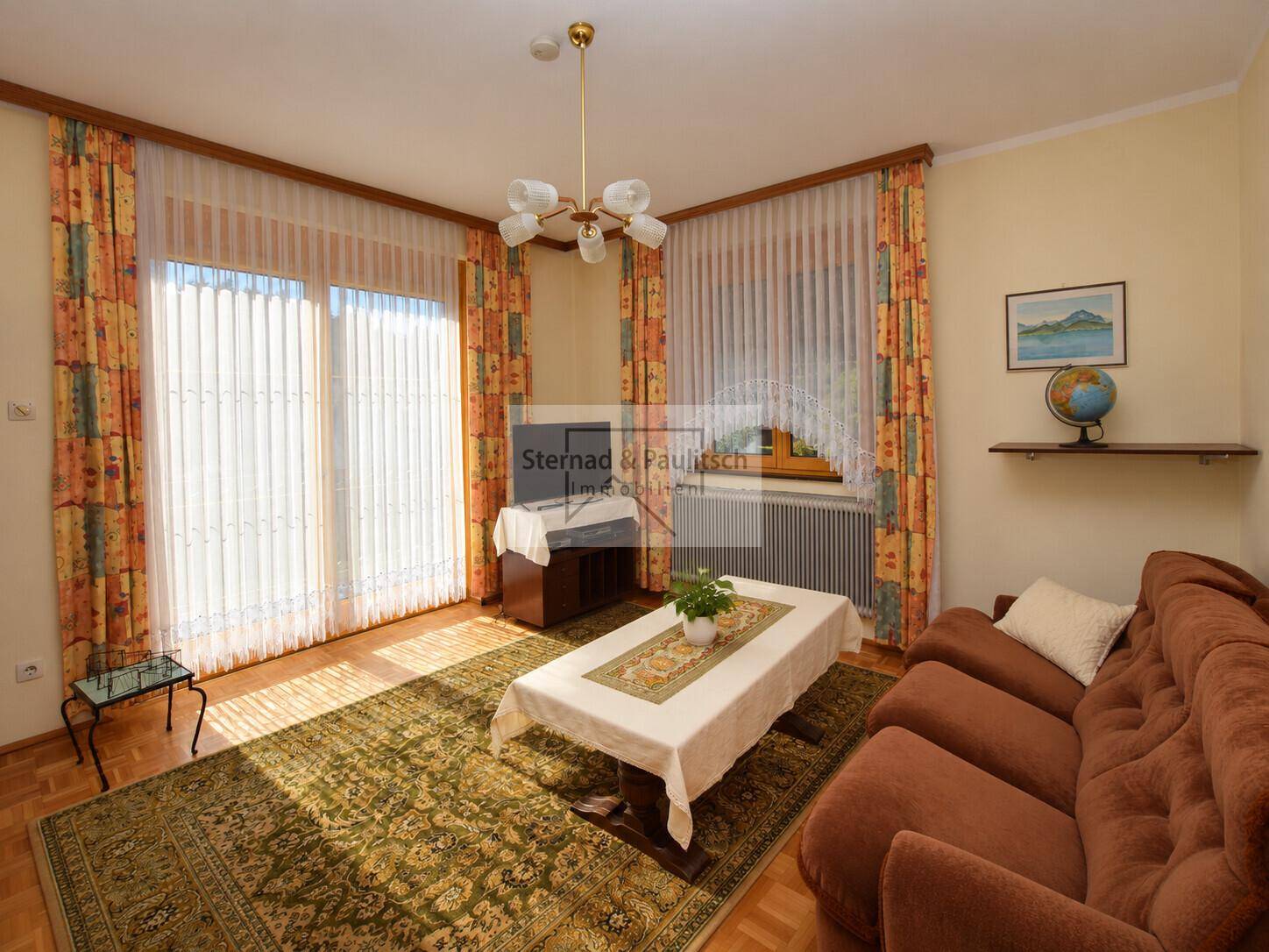 Helles Wohnzimmer mit braunem Sofa, Teppich und großem Fenster mit viel Tageslicht.