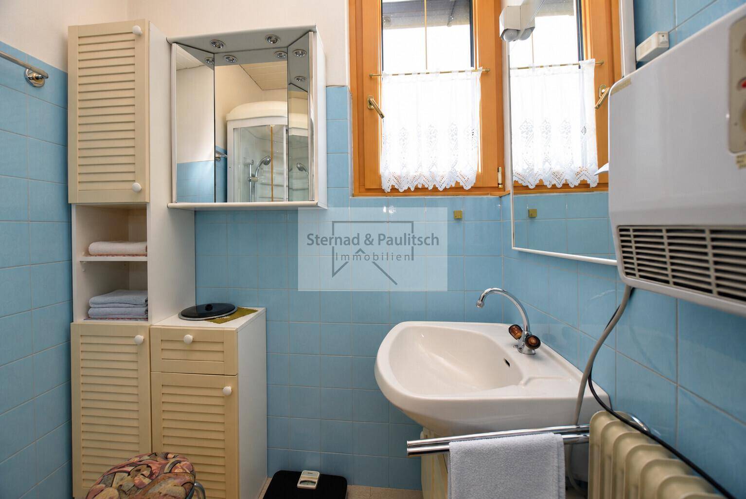 Badezimmer mit Waschbecken, Spiegelschrank und hellblauen Fliesen an den Wänden.