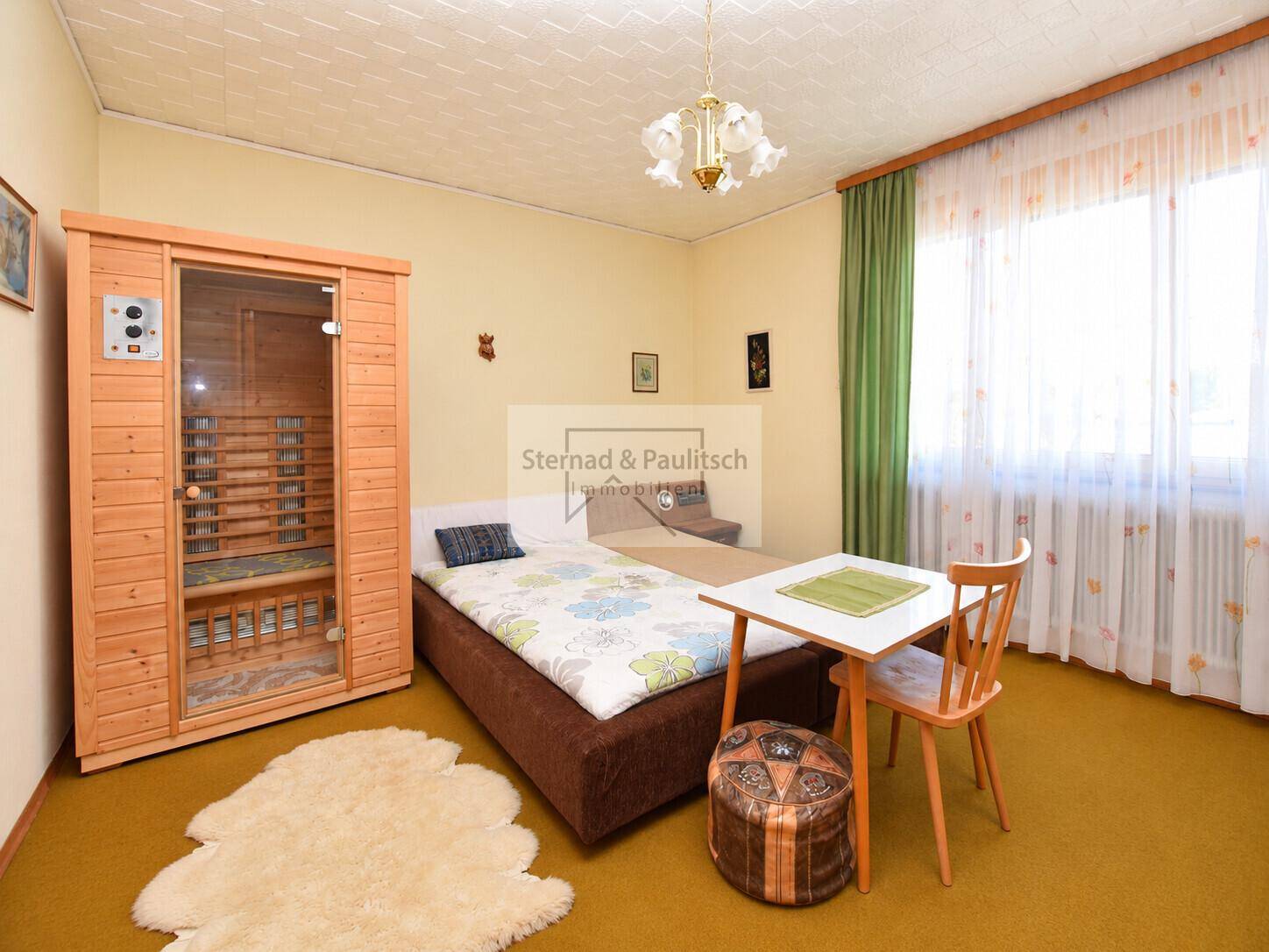 Schlafzimmer mit Einzelbett, kleinem Tisch und einer Infrarot-Saunakabine für Wellness.