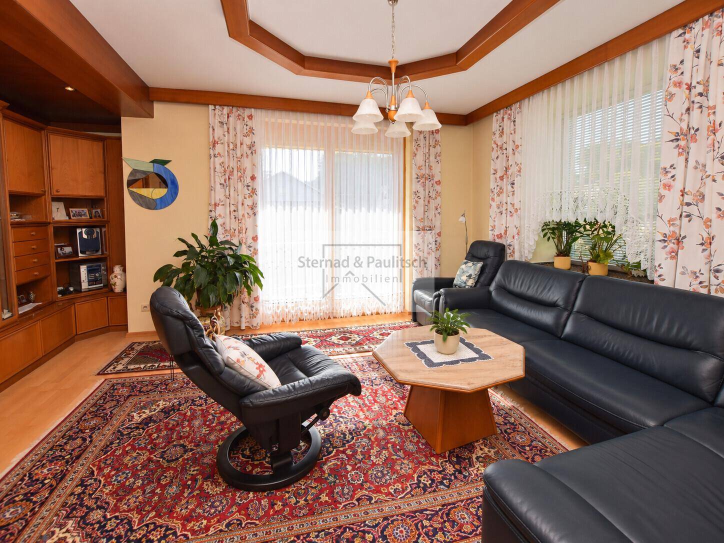 Gemütliches Wohnzimmer mit dunklen Ledersofas, traditionellem Teppich und Holzbalkendecke.