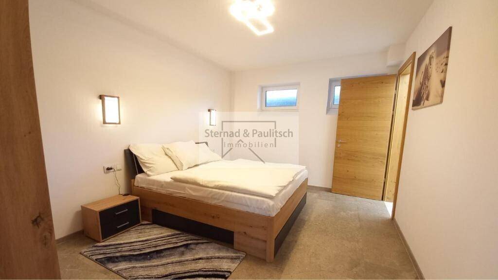 Modernes Schlafzimmer mit Holzbett, Nachttisch und zwei Fenstern für Tageslicht.