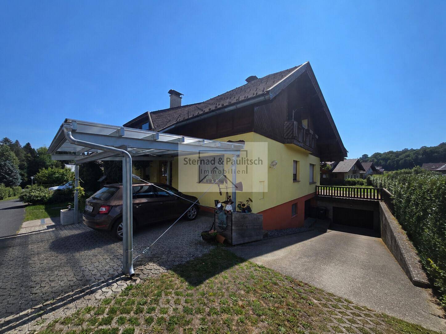 Seitenansicht des Hauses mit Carport, gepflasterter Einfahrt und Zugang zur Tiefgarage.