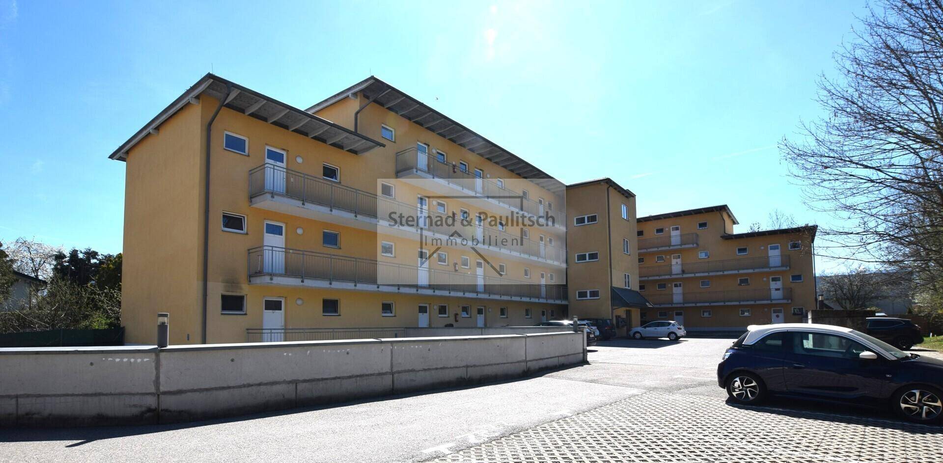 Mehrfamilienhaus mit gelber Fassade, Balkonen und Außenparkplätzen.