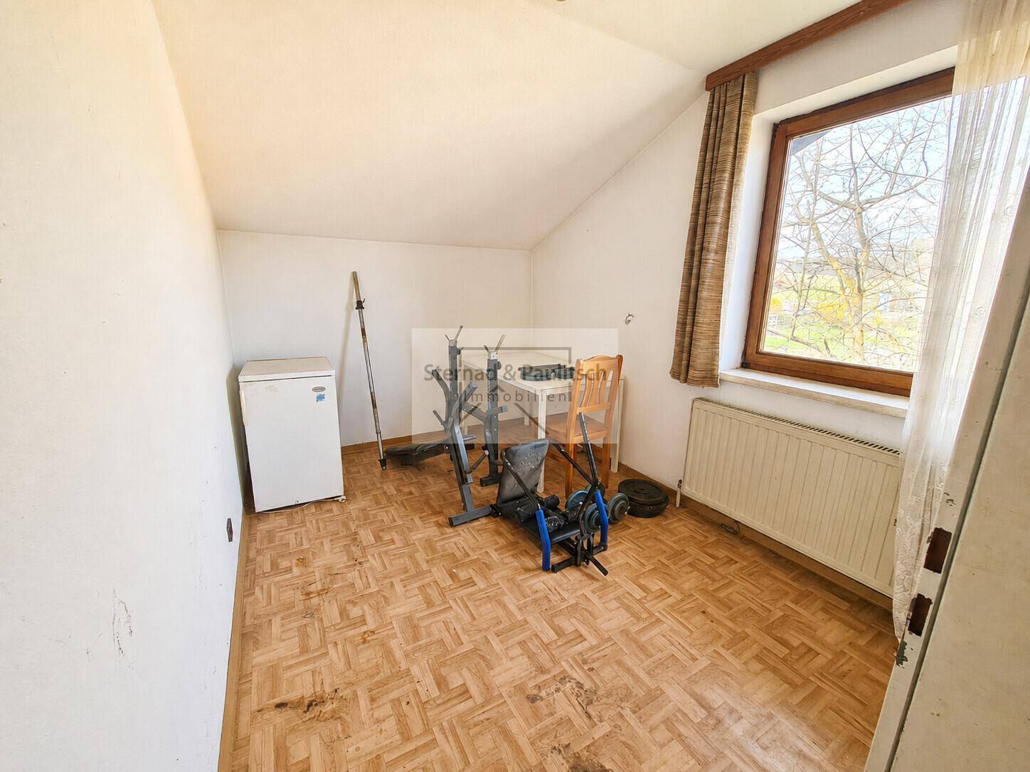 Raum mit Laminatboden, Fenster und Fitnessgeräten, ideal als kleines Home-Gym.