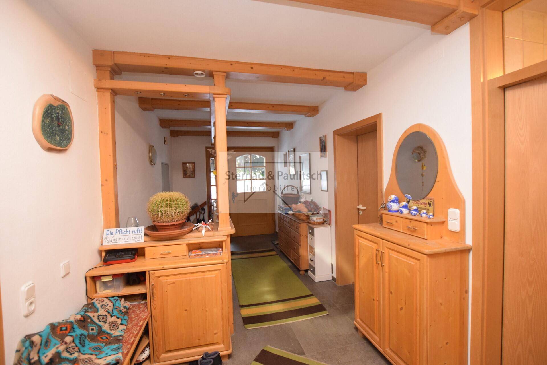 Langer Flur mit Holzmöbeln, Fliesenboden und Holzbalken an der Decke.