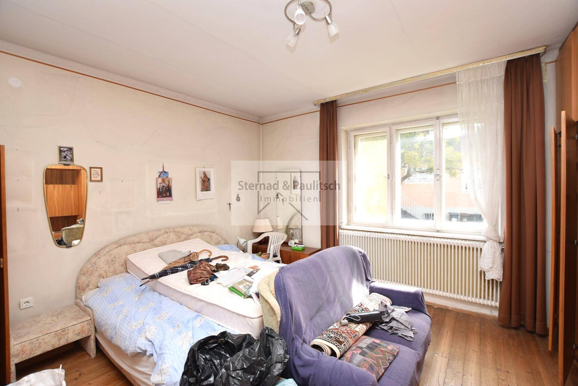Schlafzimmer mit Holzboden, großem Fenster und einem Bett mit Nachttisch.