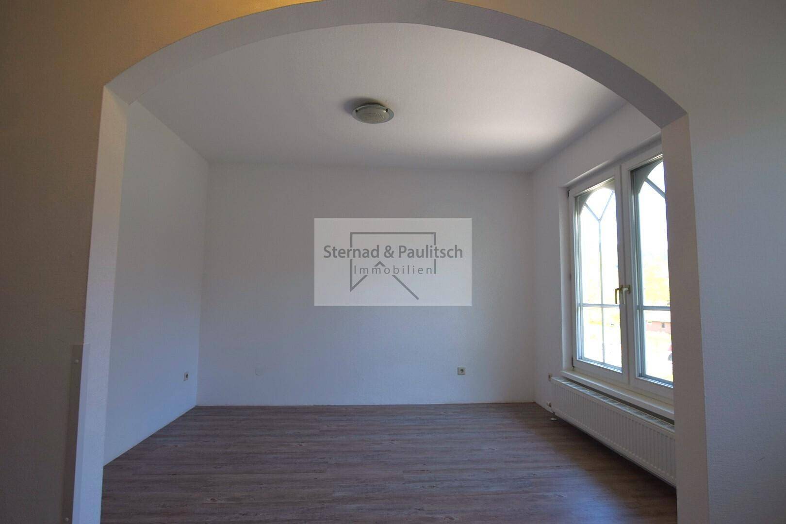 Helles Zimmer mit Holzboden und großem Fenster, vielseitig nutzbar als Schlaf- oder Arbeitszimmer.