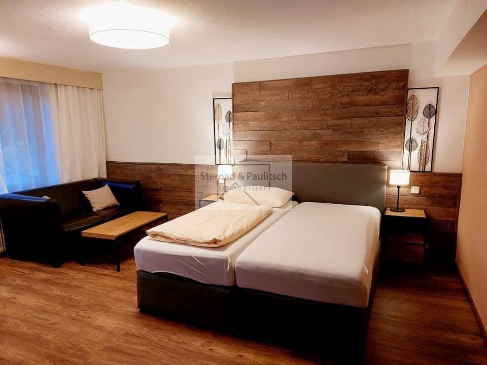 Modernes Schlafzimmer mit Doppelbett, Holzwandverkleidung und dunklem Sofa.