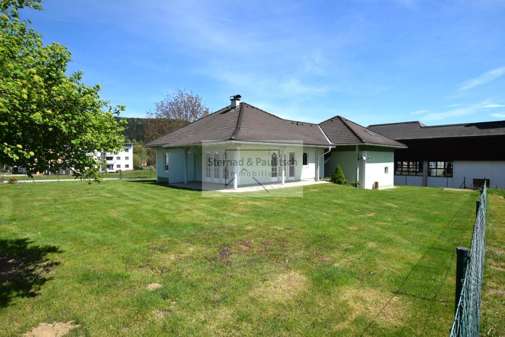 Weitläufiger Gartenbereich mit Blick auf das Einfamilienhaus unter strahlend blauem Himmel.