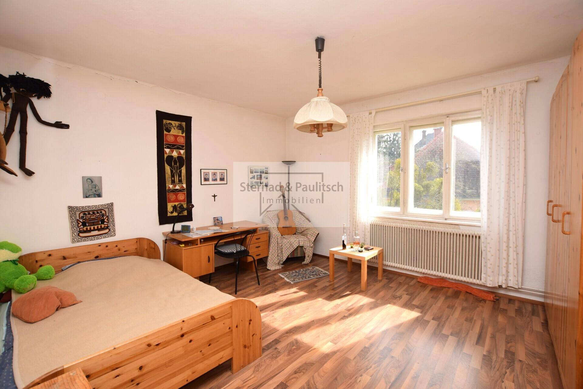 Schlafzimmer mit Holzboden, Schreibtisch und einem großen Fenster.