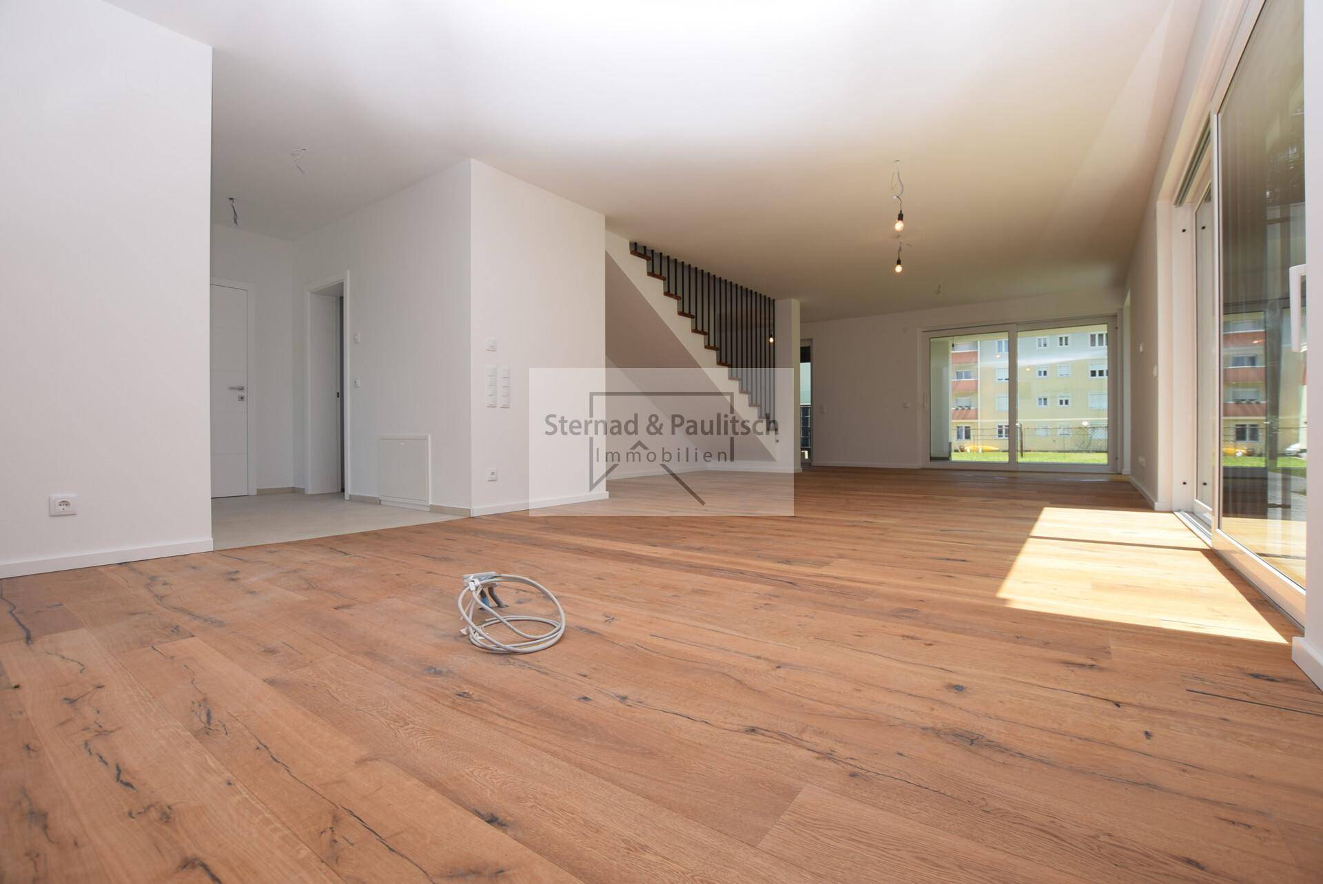 Geräumiger, unmöblierter Wohnbereich mit Holzboden und viel Tageslicht durch große Schiebetüren.