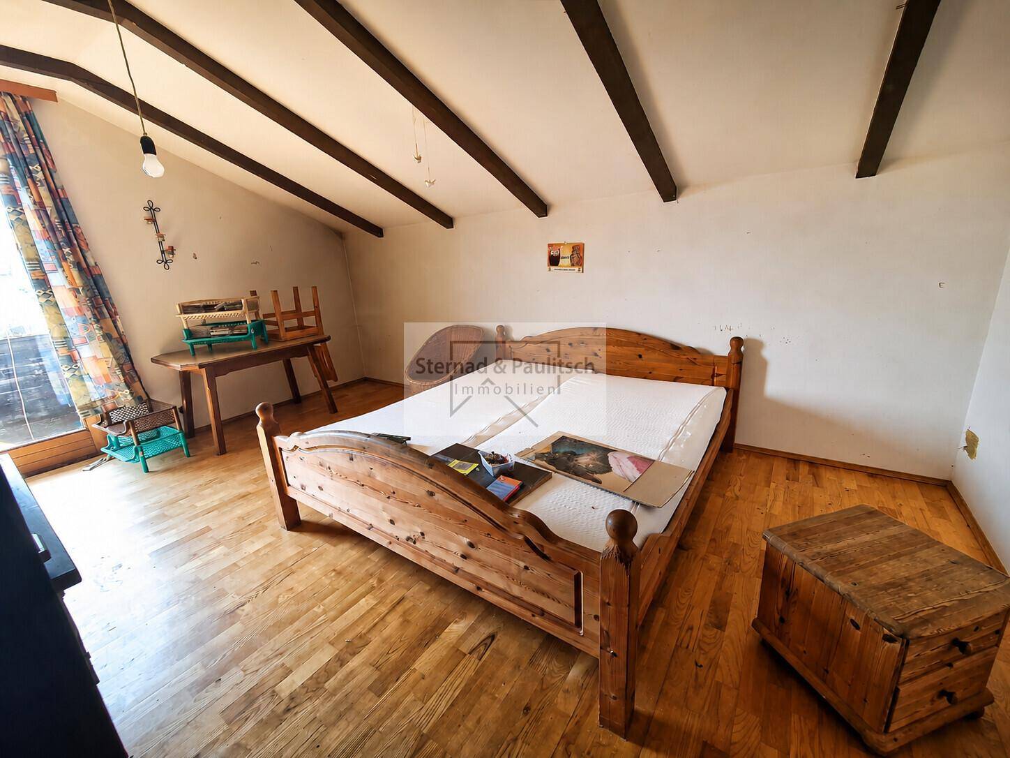 Rustikales Schlafzimmer mit Holzbalken, Holzboden und Zugang zum Balkon.