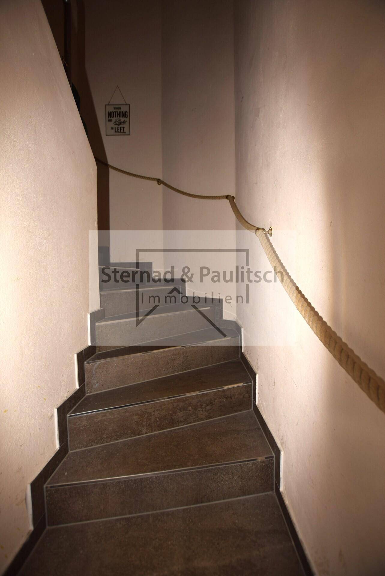 Treppenhaus mit gefliesten Stufen und Seilgeländer, führt in die oberen Etagen.