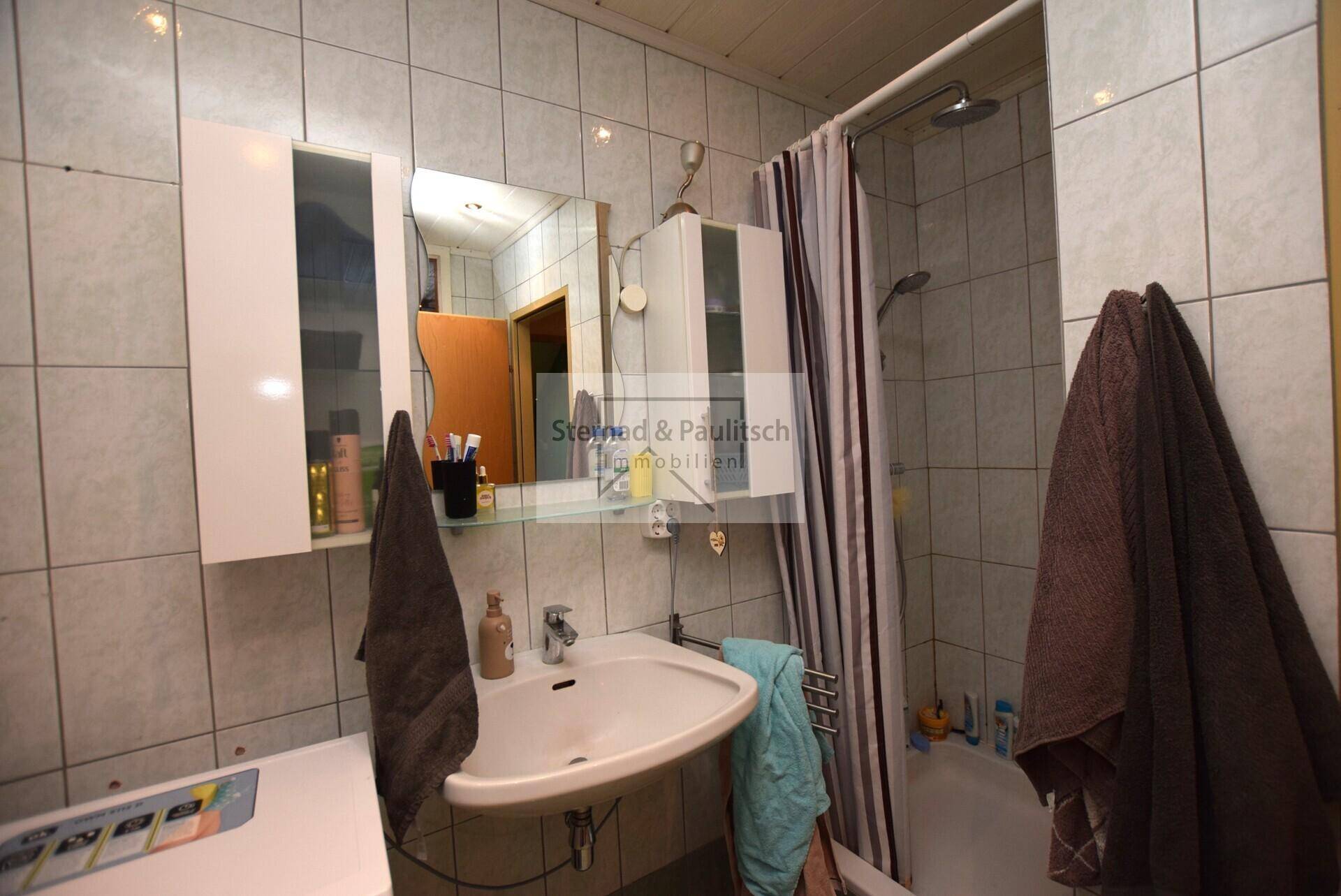 Badezimmer mit Duschbereich, Waschbecken und Spiegelschrank, gefliest und funktional.