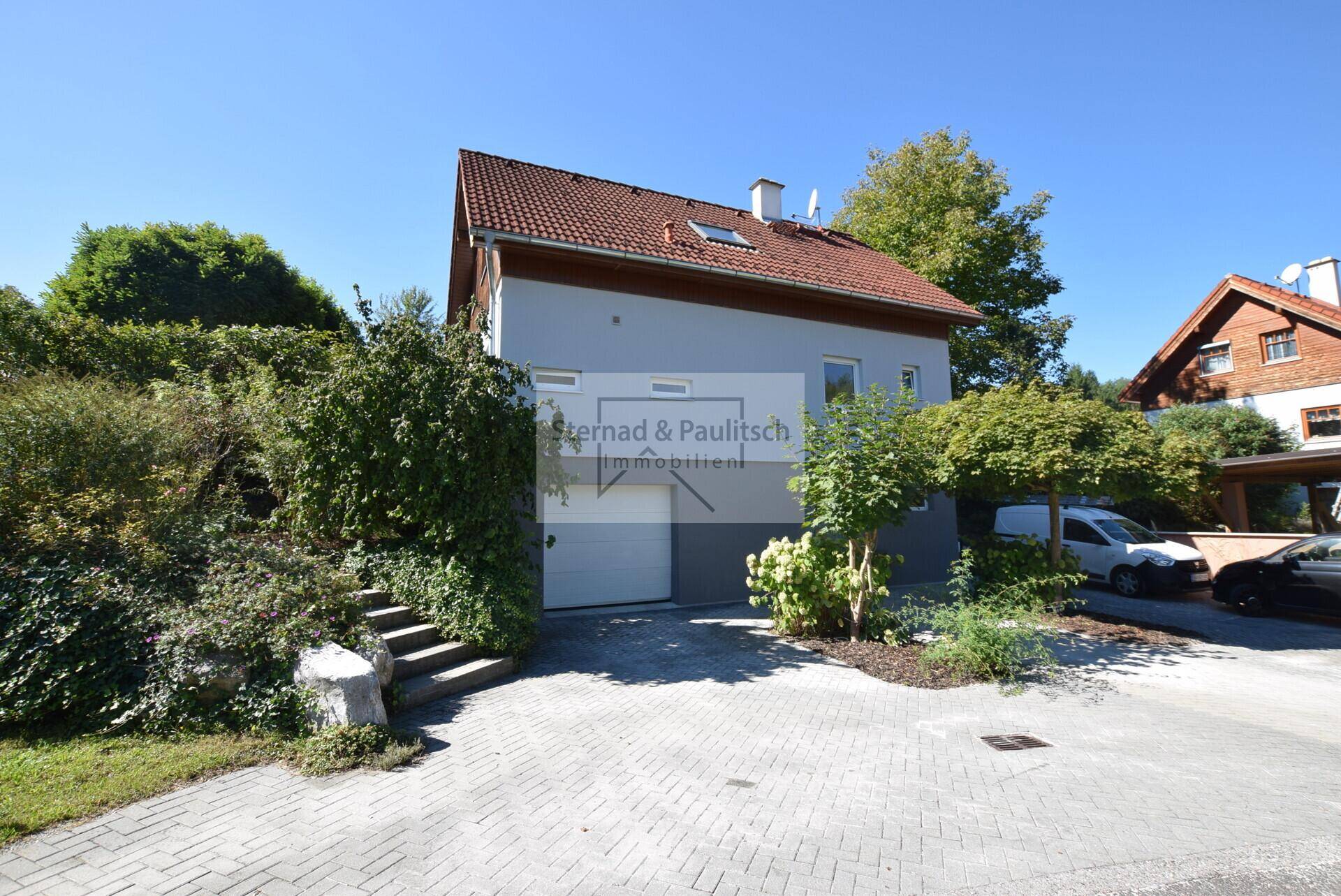 Vorderansicht des Hauses mit Zufahrt, integrierter Garage und gepflegter Bepflanzung.