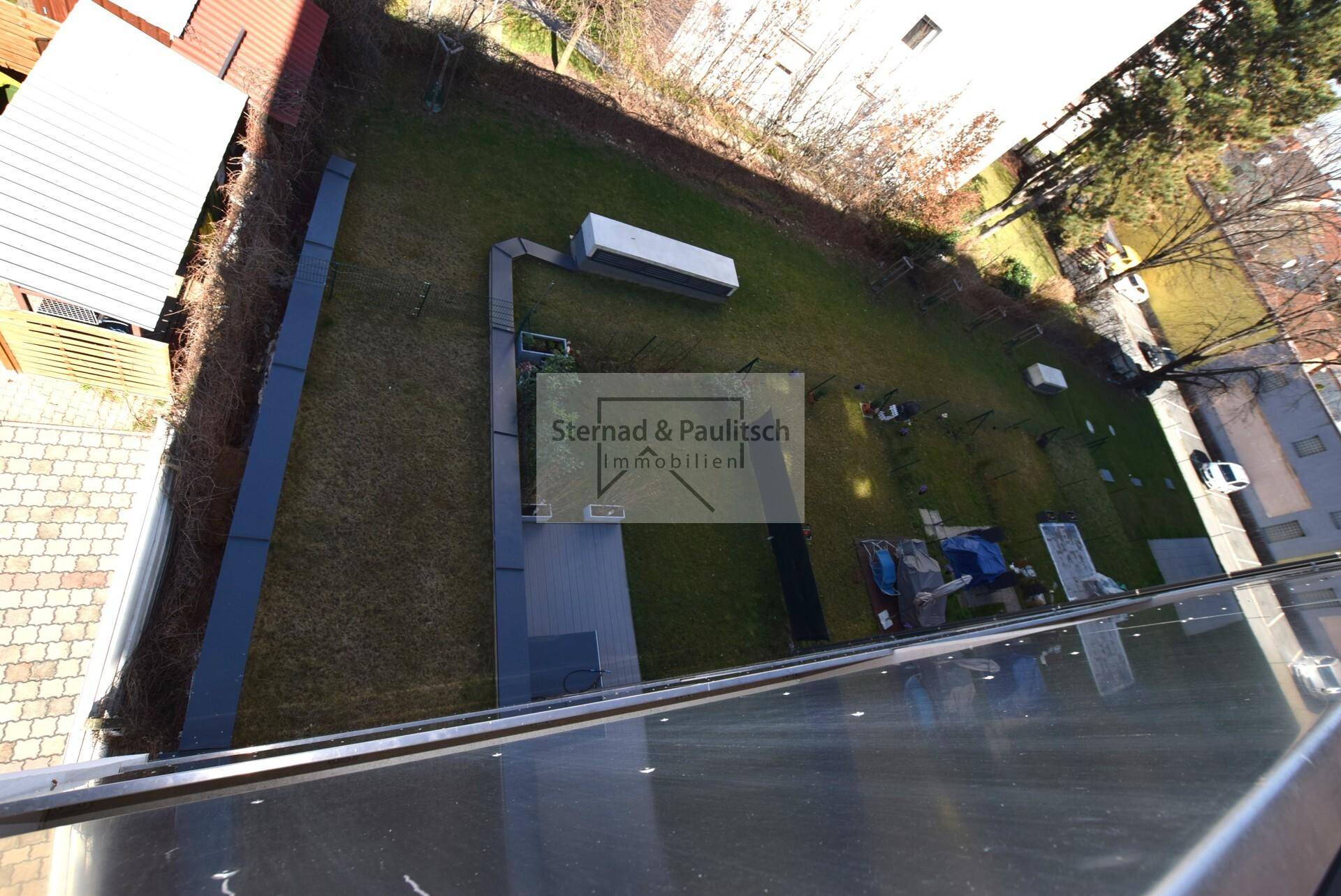 Vogelperspektive auf den Gartenbereich mit Rasenfläche und angrenzenden Gebäuden, bietet Grünblick.