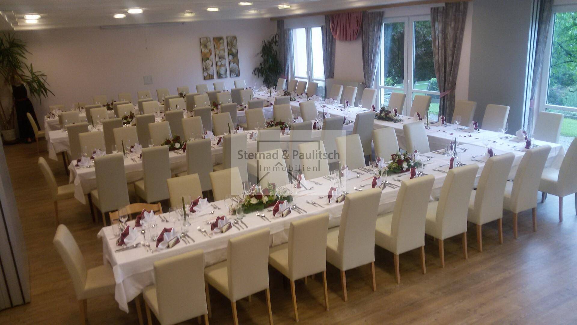Großer Speisesaal mit langen Tischen, elegant gedeckt für eine Veranstaltung und großen Fenstern.