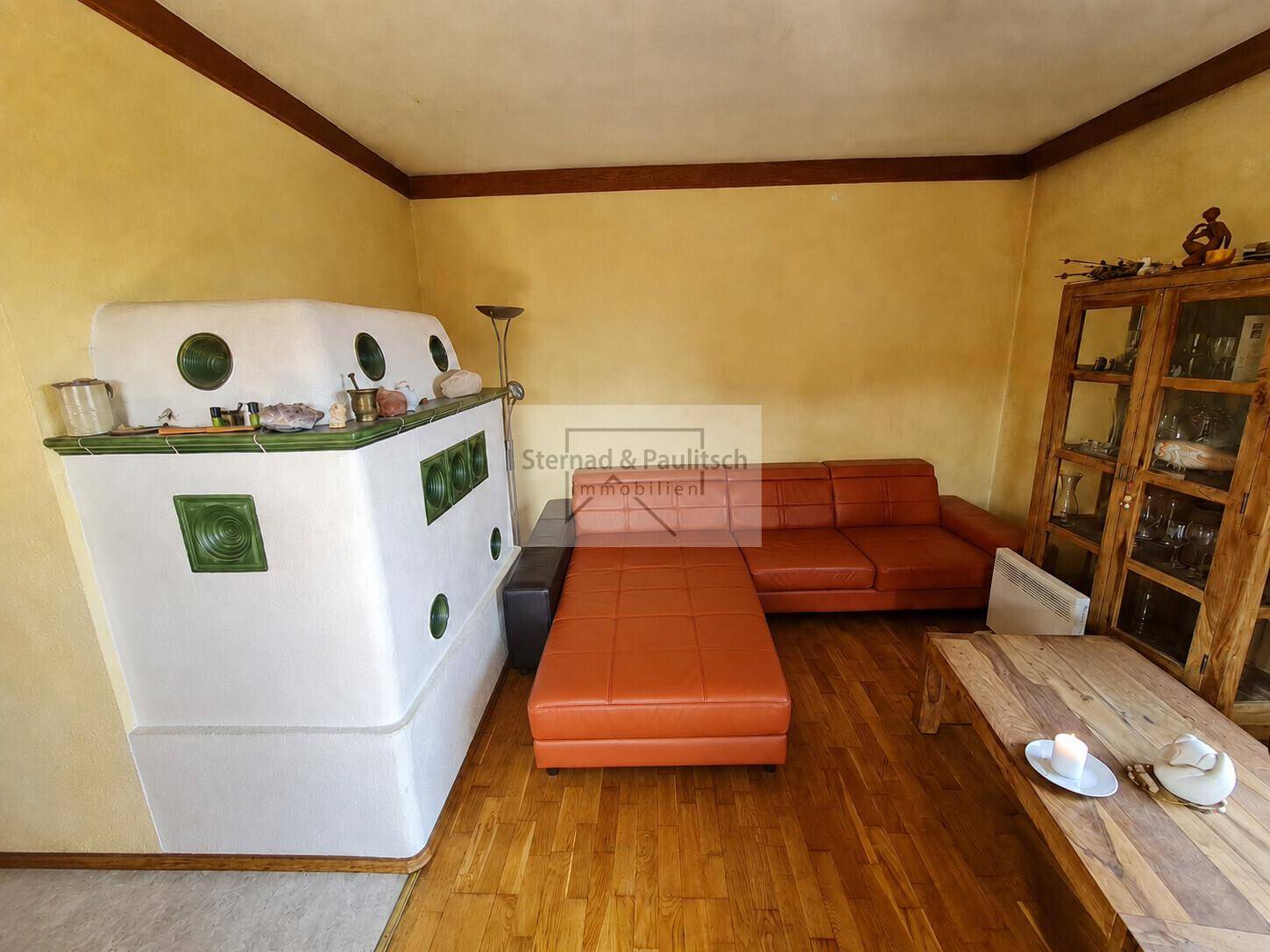 Helles Wohnzimmer mit traditionellem Kachelofen, bequemer Couch und Holzmöbeln.