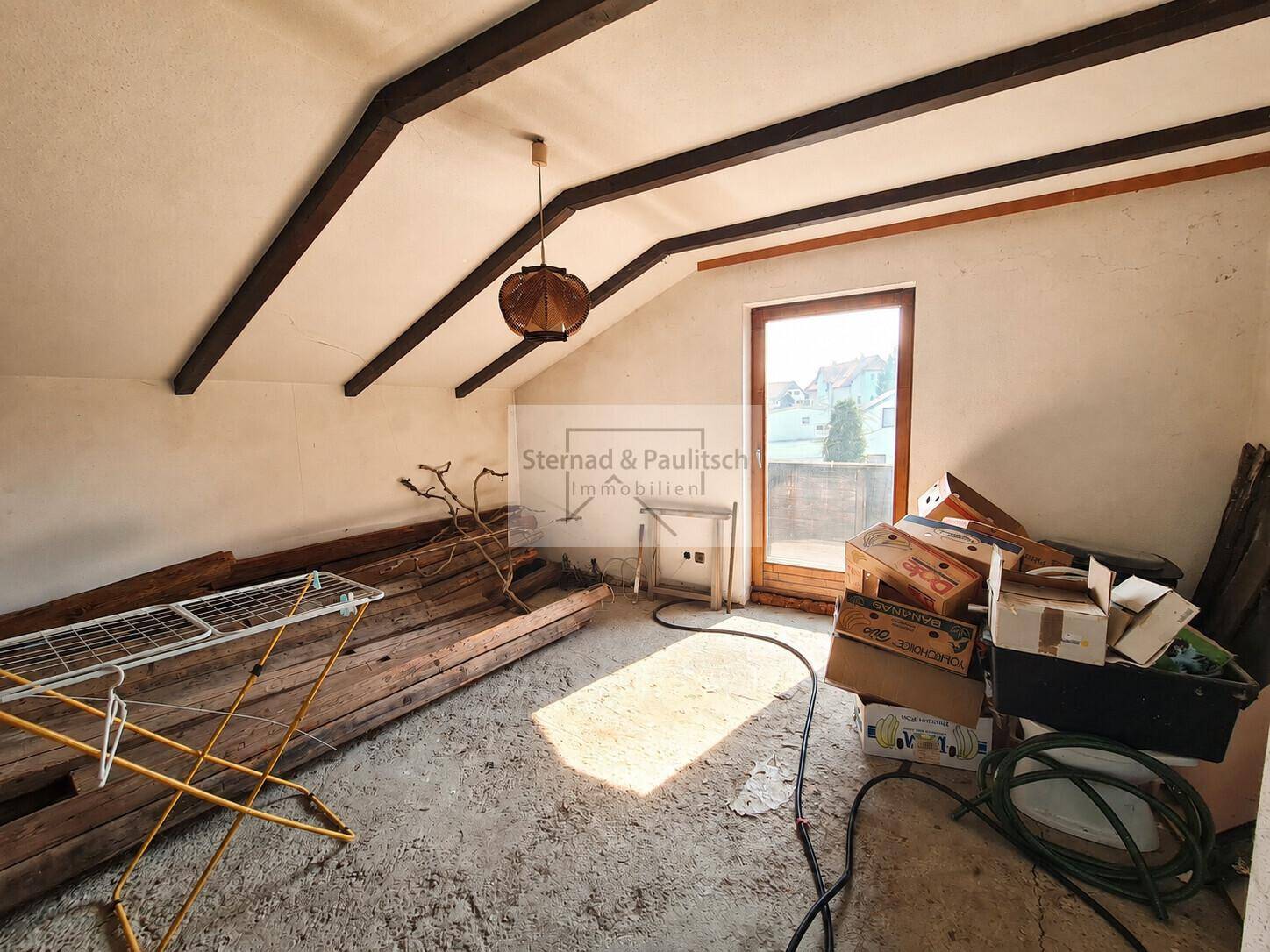 Dachbodenraum mit sichtbaren Holzbalken und Zugang zu einem kleinen Balkon.