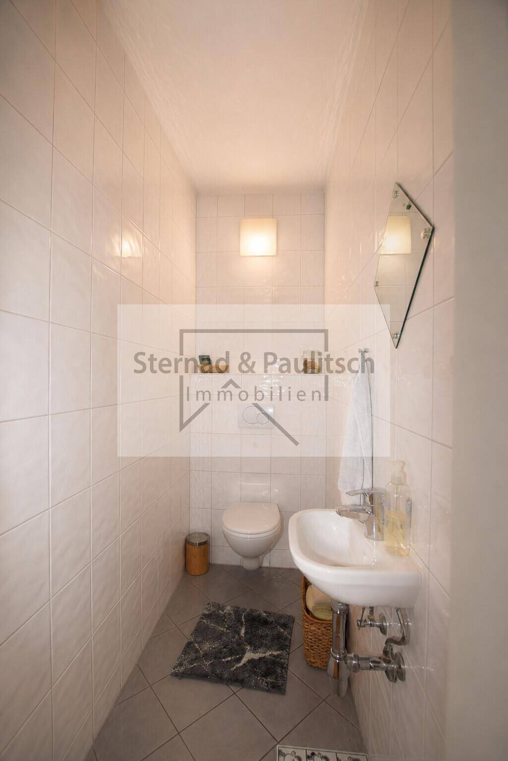 Kleines Gäste-WC mit Toilette und Waschbecken, komplett gefliest und funktional eingerichtet.