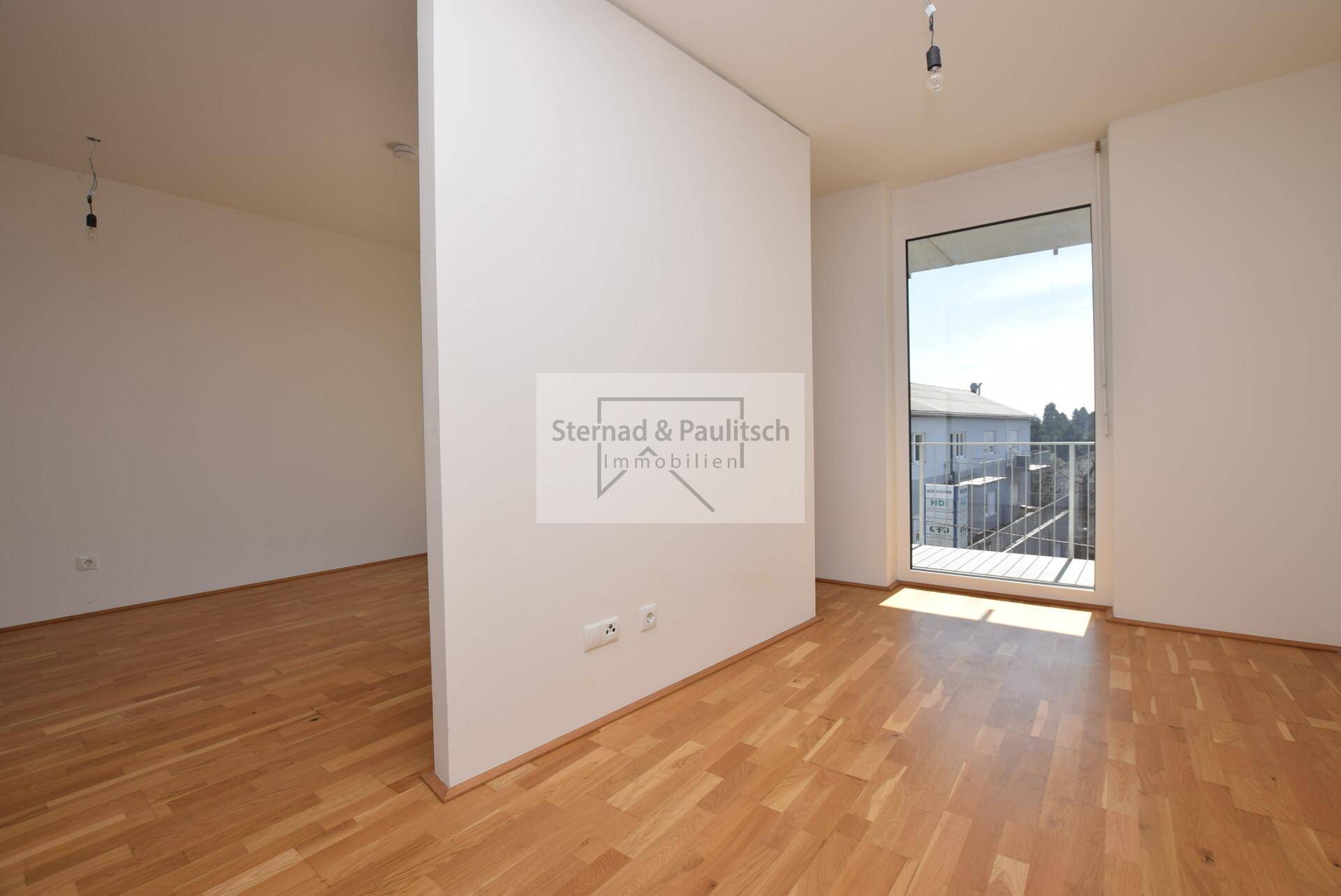 Heller Wohnbereich mit Parkettboden und Zugang zu einem sonnigen Balkon, offen gestaltet.