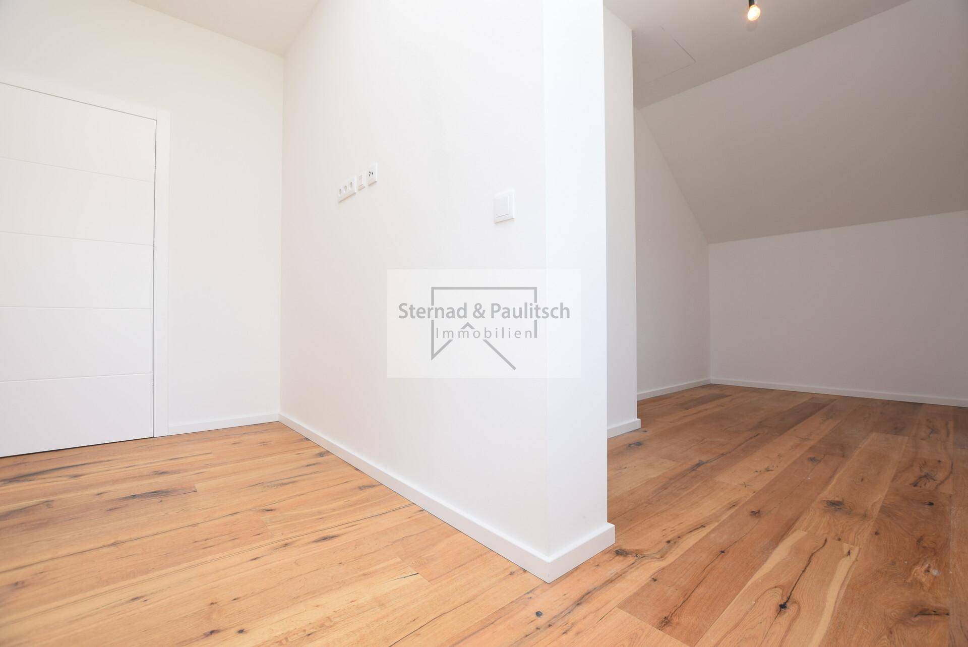 Unmöbliertes Zimmer mit Holzboden, Dachschräge und weiß gestrichenen Wänden.