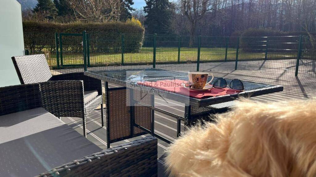 Sonnige Terrasse mit modernen Gartenmöbeln und Blick auf die grüne Umgebung.