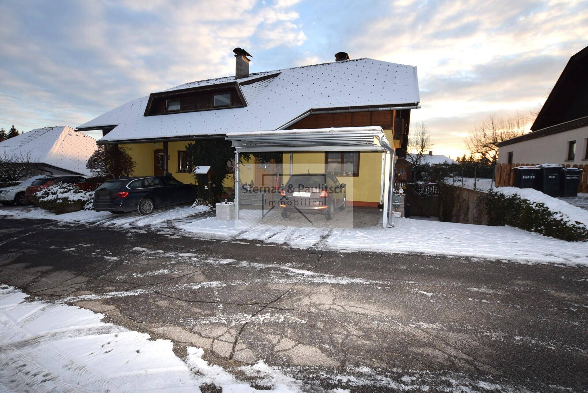 Hausansicht im Winter mit schneebedeckter Straße, Carport und geparktem Auto.