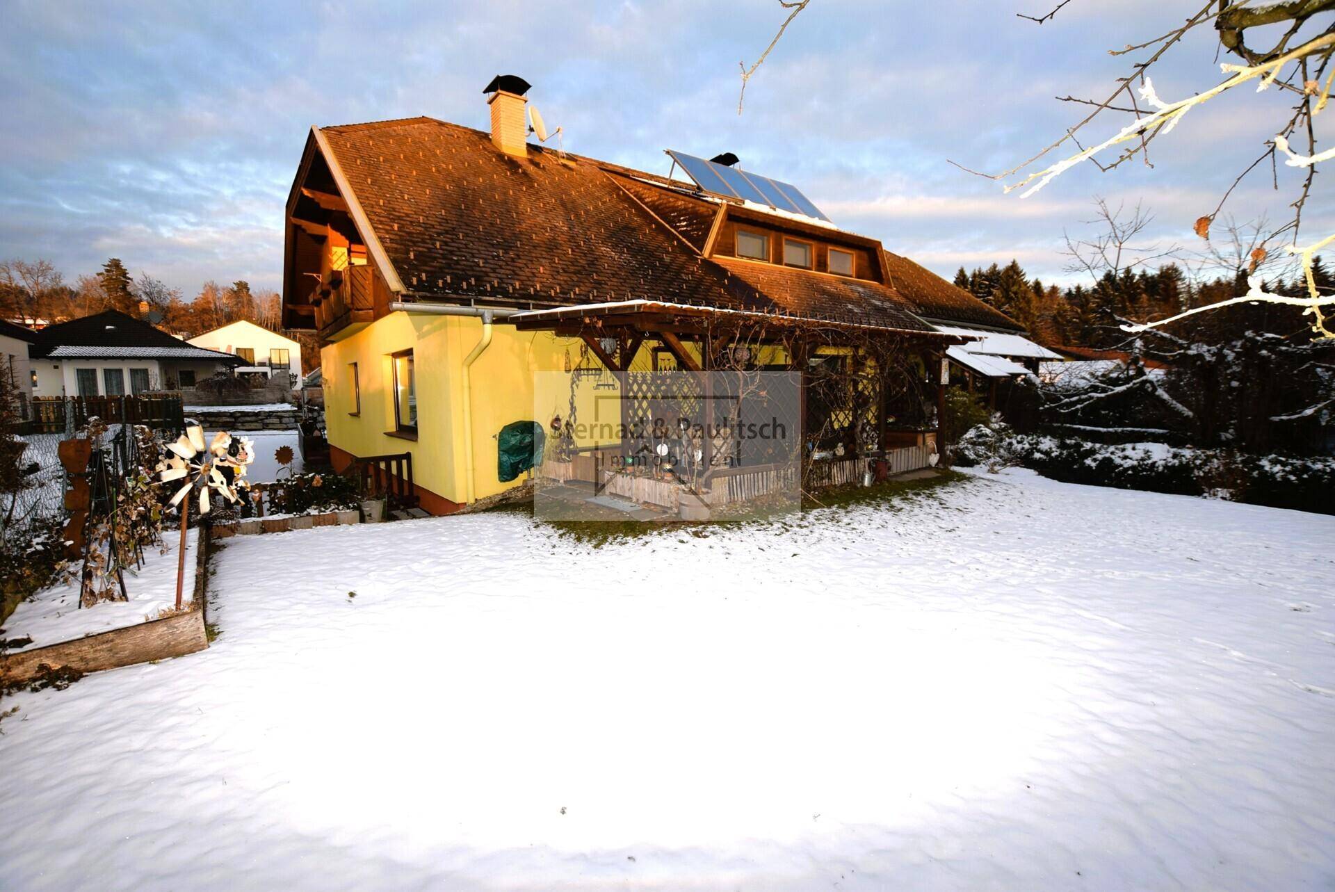 Winterliche Ansicht des Hauses mit schneebedecktem Garten, gelber Fassade und Solaranlage.