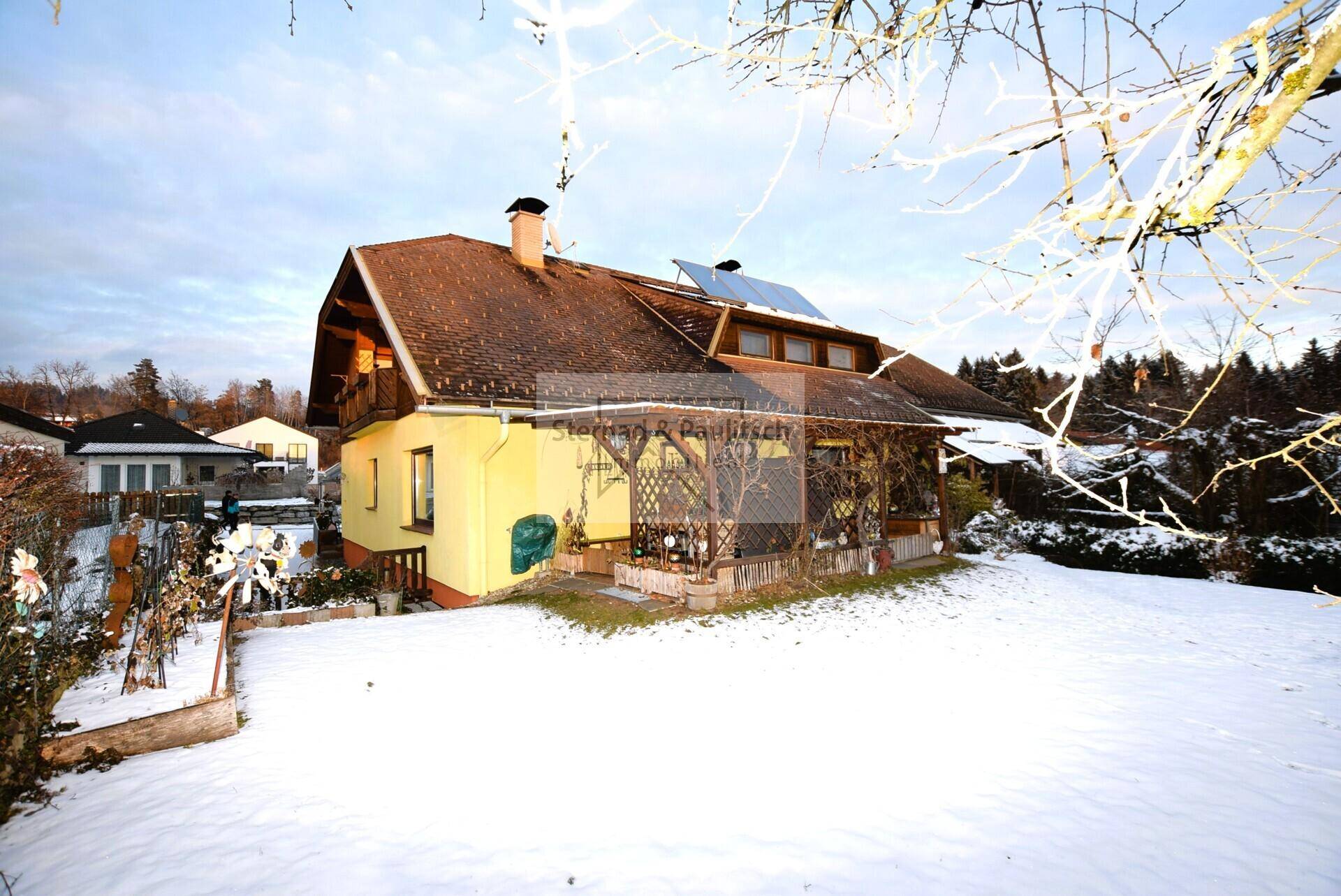 Winterliche Ansicht des Hauses mit schneebedecktem Garten, gelber Fassade und Solaranlage.