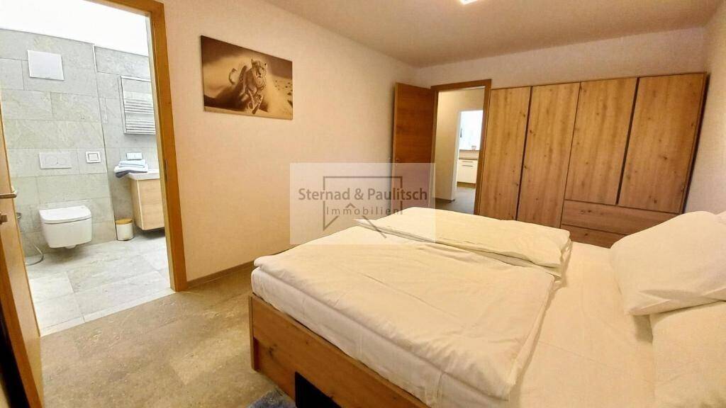 Schlafzimmer mit Holzkleiderschrank und direktem Zugang zu einem modernen Badezimmer.