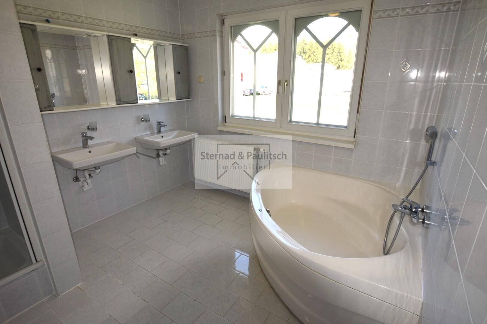 Geräumiges Badezimmer mit Badewanne, Doppelwaschbecken und großem Fenster.