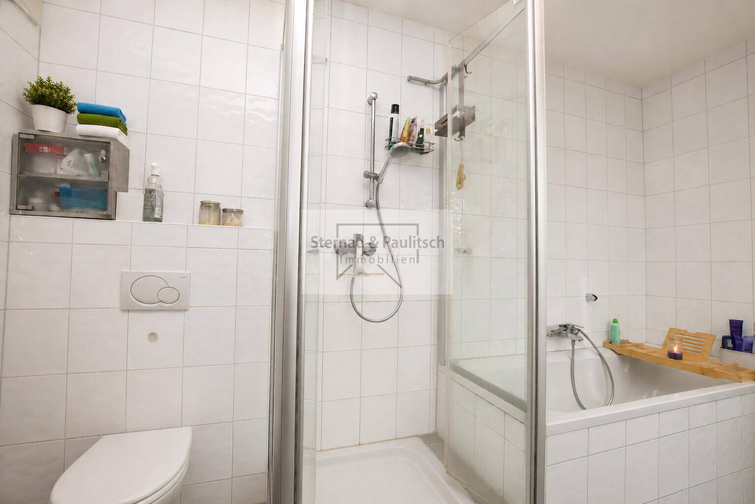 Badezimmer mit Badewanne, Duschkabine und Toilette, komplett gefliest und gut beleuchtet.