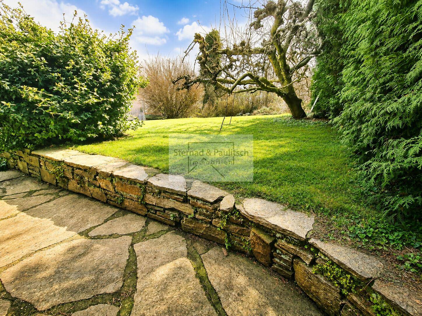 Gepflegter Gartenbereich mit Natursteinmauer und weitläufiger Rasenfläche.