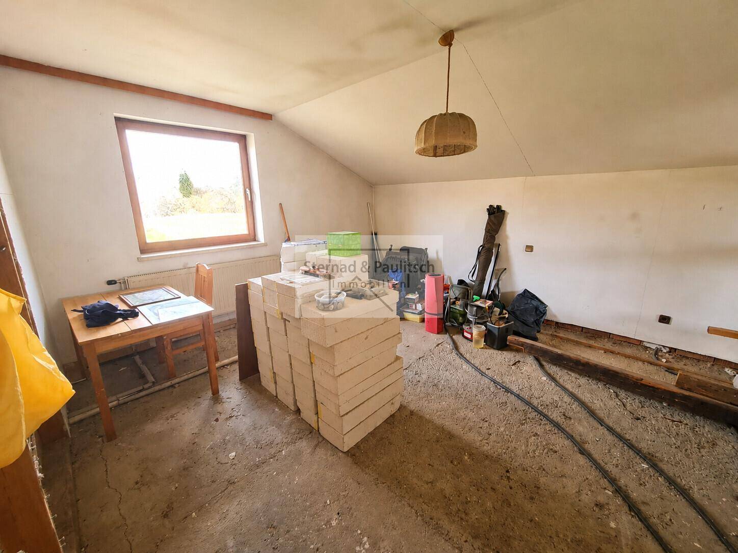 Unausgebauter Dachbodenraum mit Fenster und gelagerten Baumaterialien.