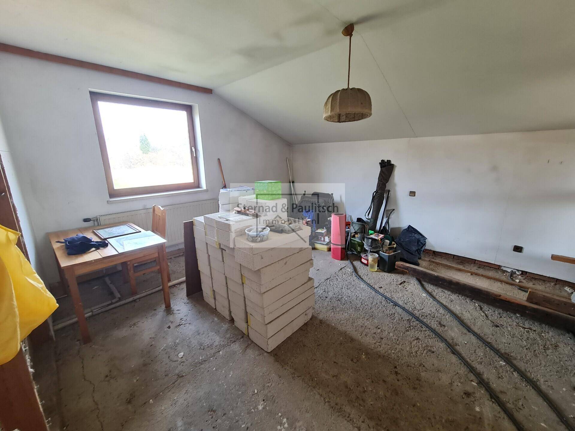 Raum mit Dachschräge und Fenster, derzeit als Lagerfläche genutzt und renovierungsbedürftig.