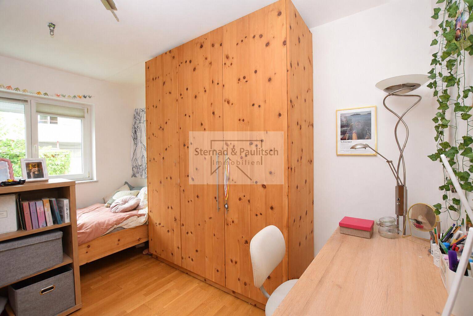 Kinderzimmer mit Holzbett, Schreibtisch und großem Kleiderschrank, hell und funktional eingerichtet.