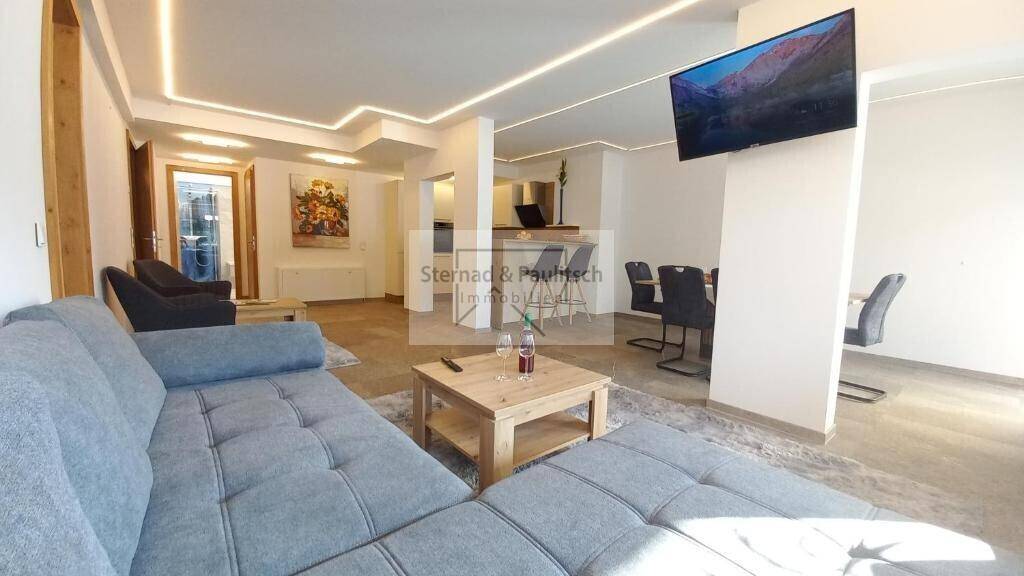 Offener Wohn- und Essbereich mit bequemer Couch, Esstisch und moderner Beleuchtung, ideal für Geselligkeit.