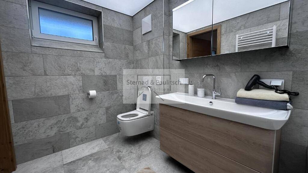 Modernes Badezimmer mit grauen Fliesen, Waschtisch und wandhängendem WC.