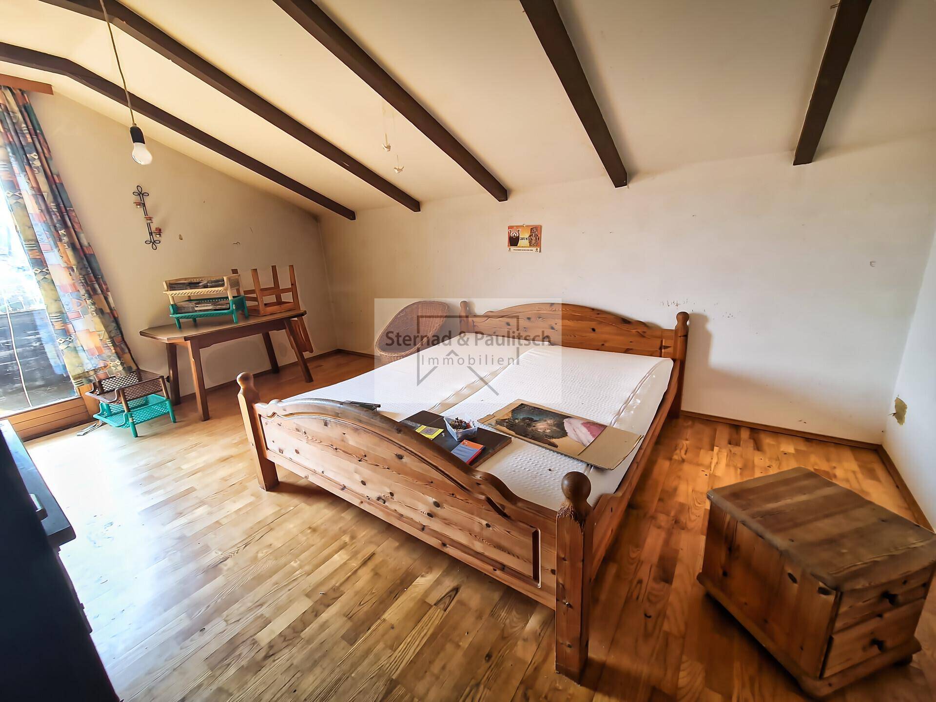 Schlafzimmer mit Holzbalkendecke, Holzbett und Parkettboden, renovierungsbedürftig.
