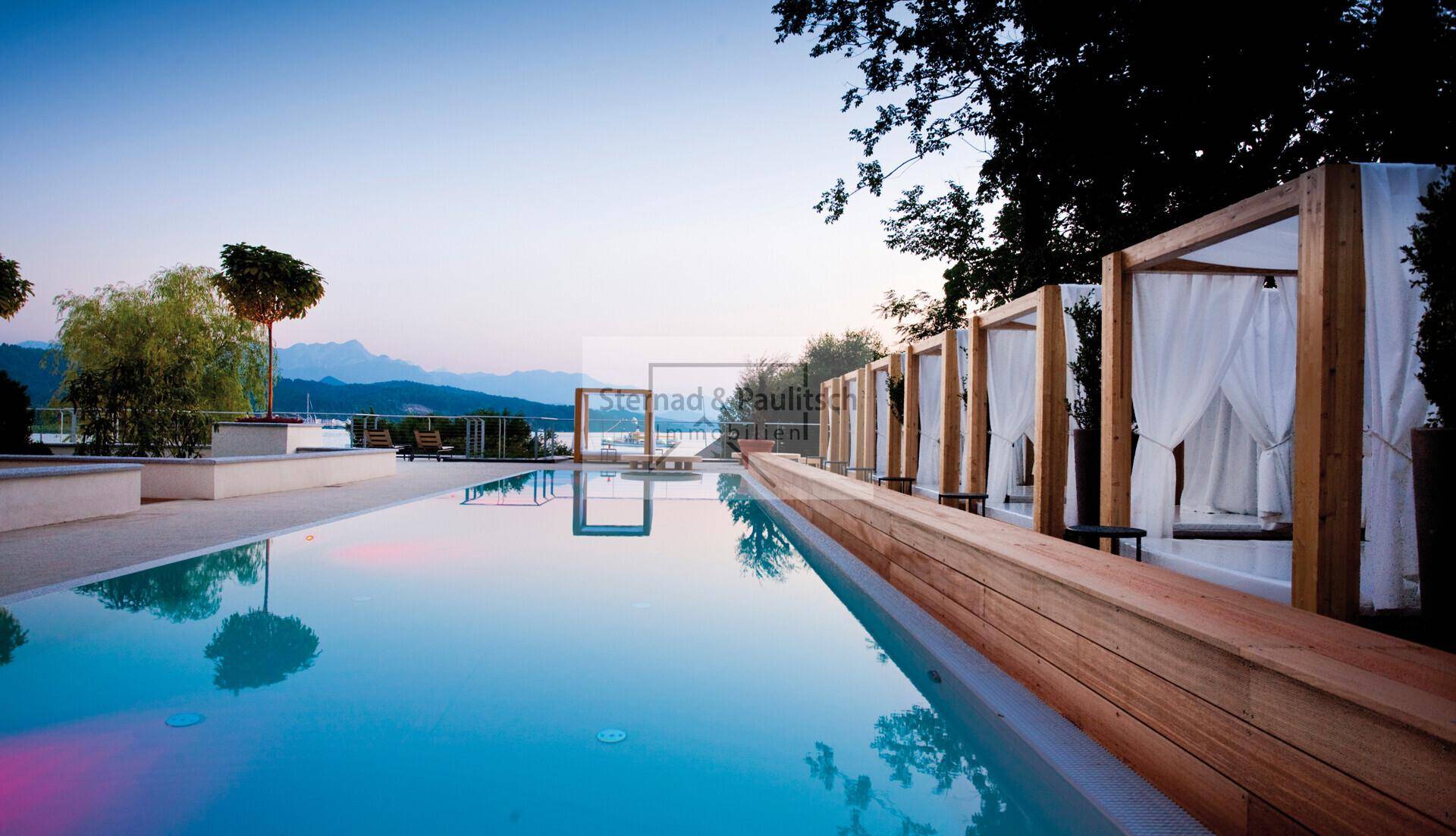 Stimmungsvoller Infinity-Pool bei Sonnenuntergang mit luxuriösen Tagesbetten und Seeblick.