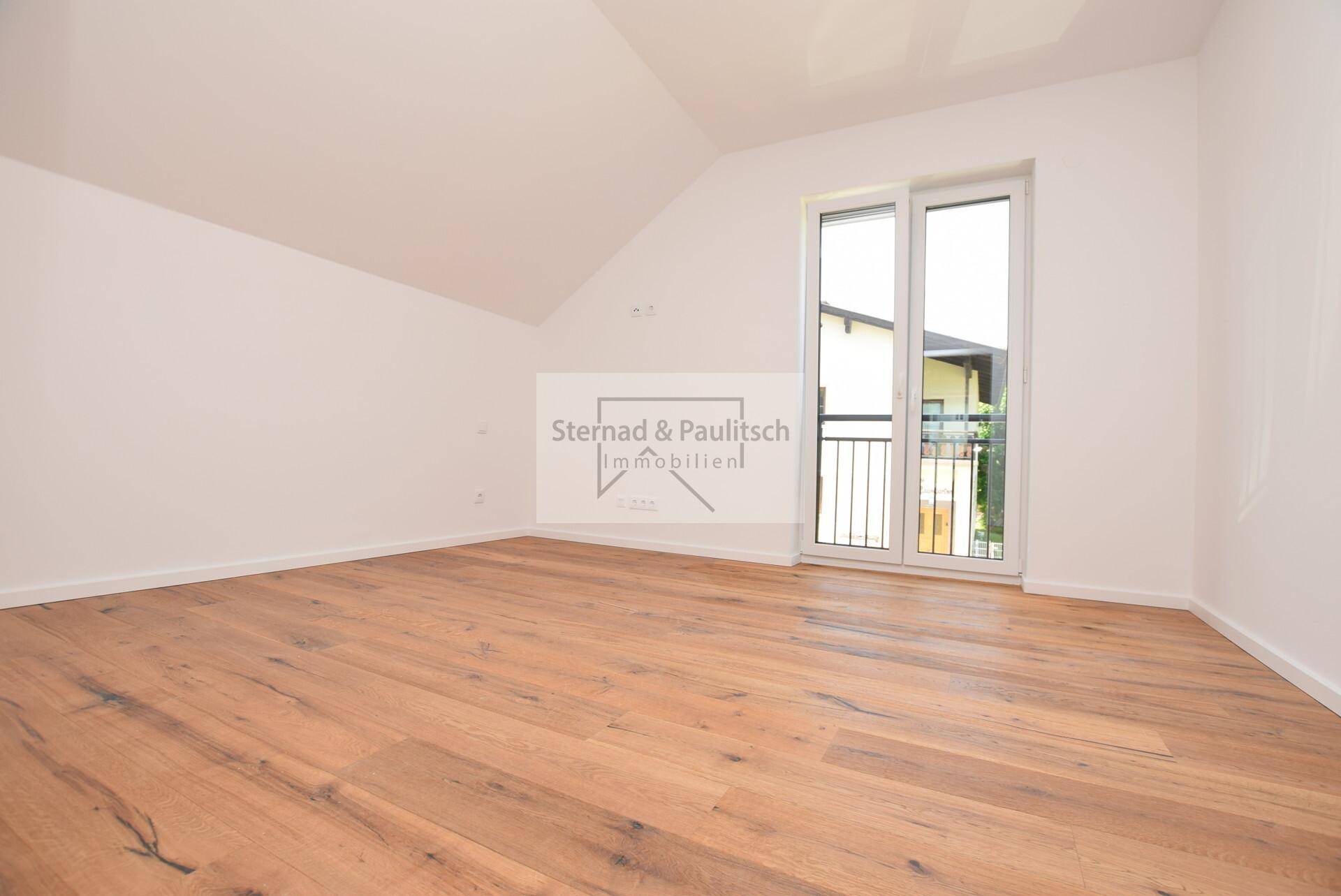 Helles, unmöbliertes Schlafzimmer mit Holzboden, Dachschräge und französischem Balkon.