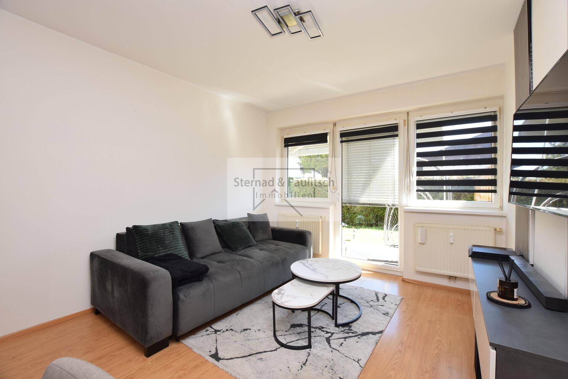 Gemütliches Wohnzimmer mit grauem Sofa, Couchtischen und Laminatboden.