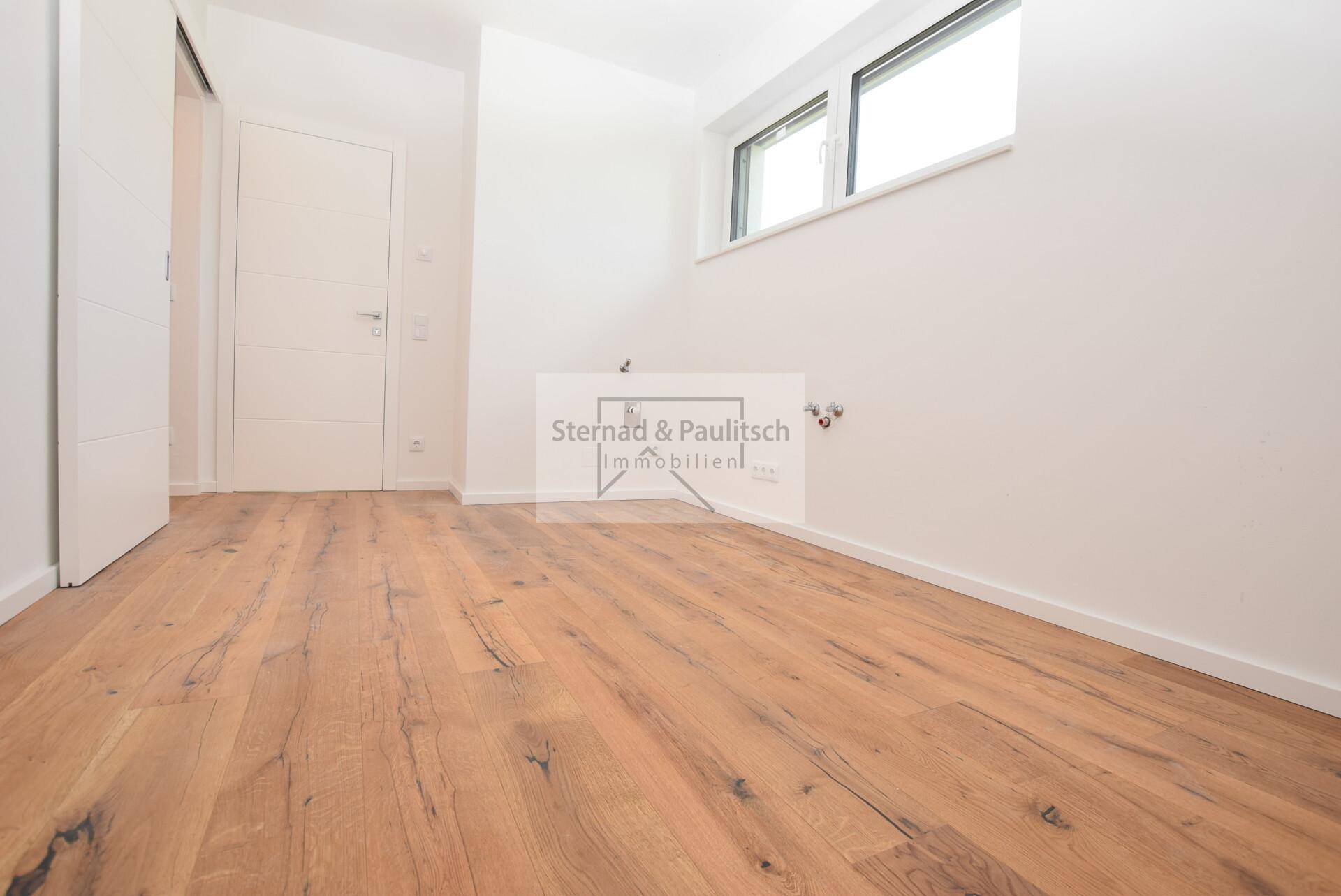 Kleiner Raum mit Holzboden und Anschlüssen, ideal als Hauswirtschaftsraum nutzbar.