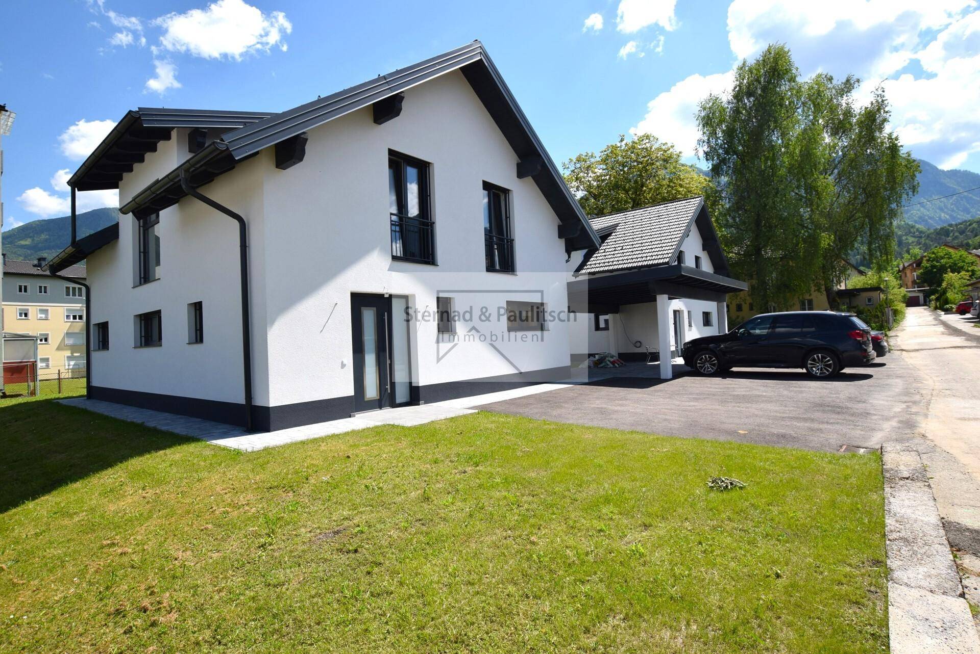 Modernes Einfamilienhaus mit Carport, gepflegtem Vorgarten und Bergblick.