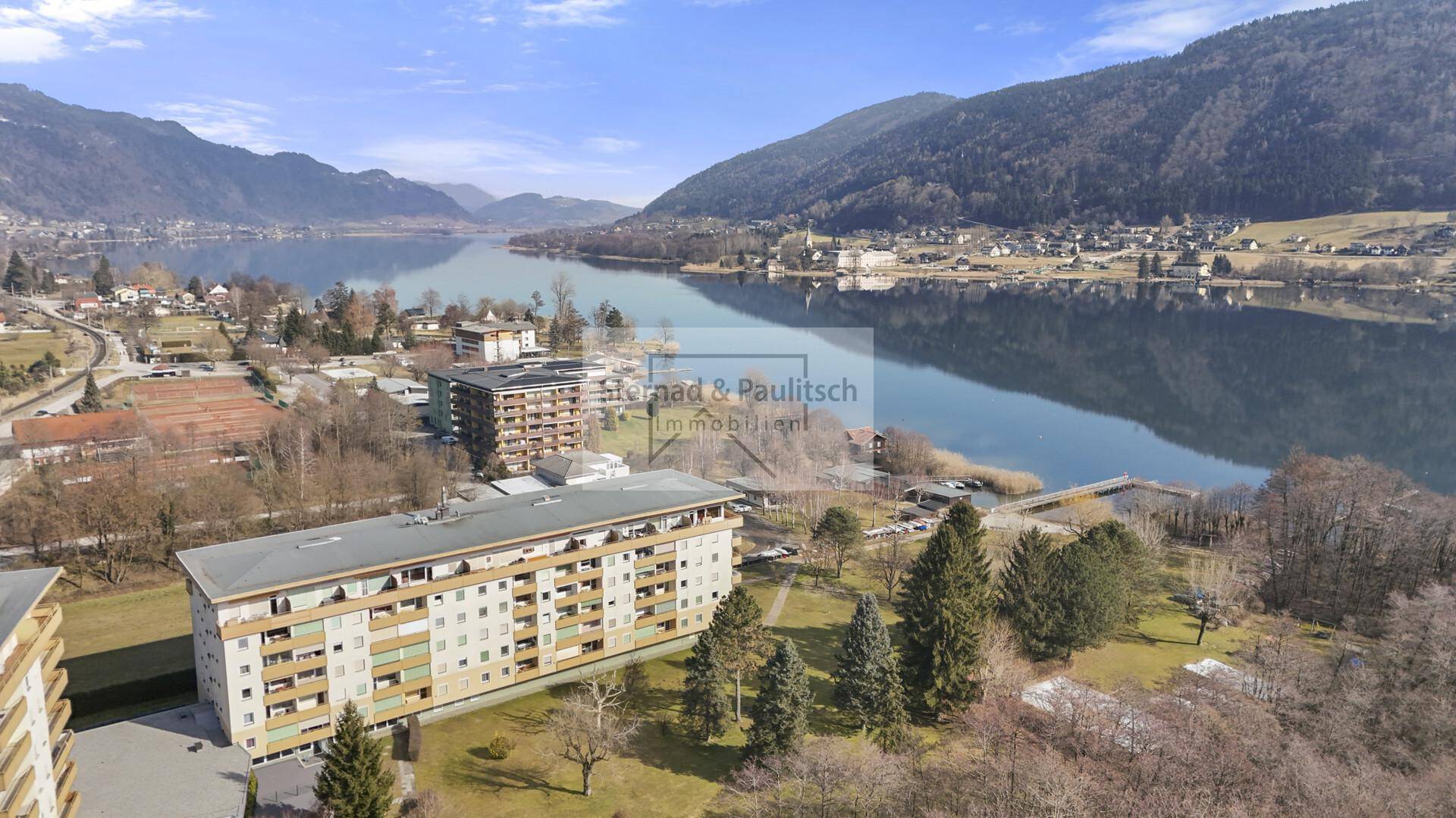 Luftaufnahme von Wohngebäuden am Seeufer mit majestätischer Bergkulisse und weitem Blick.