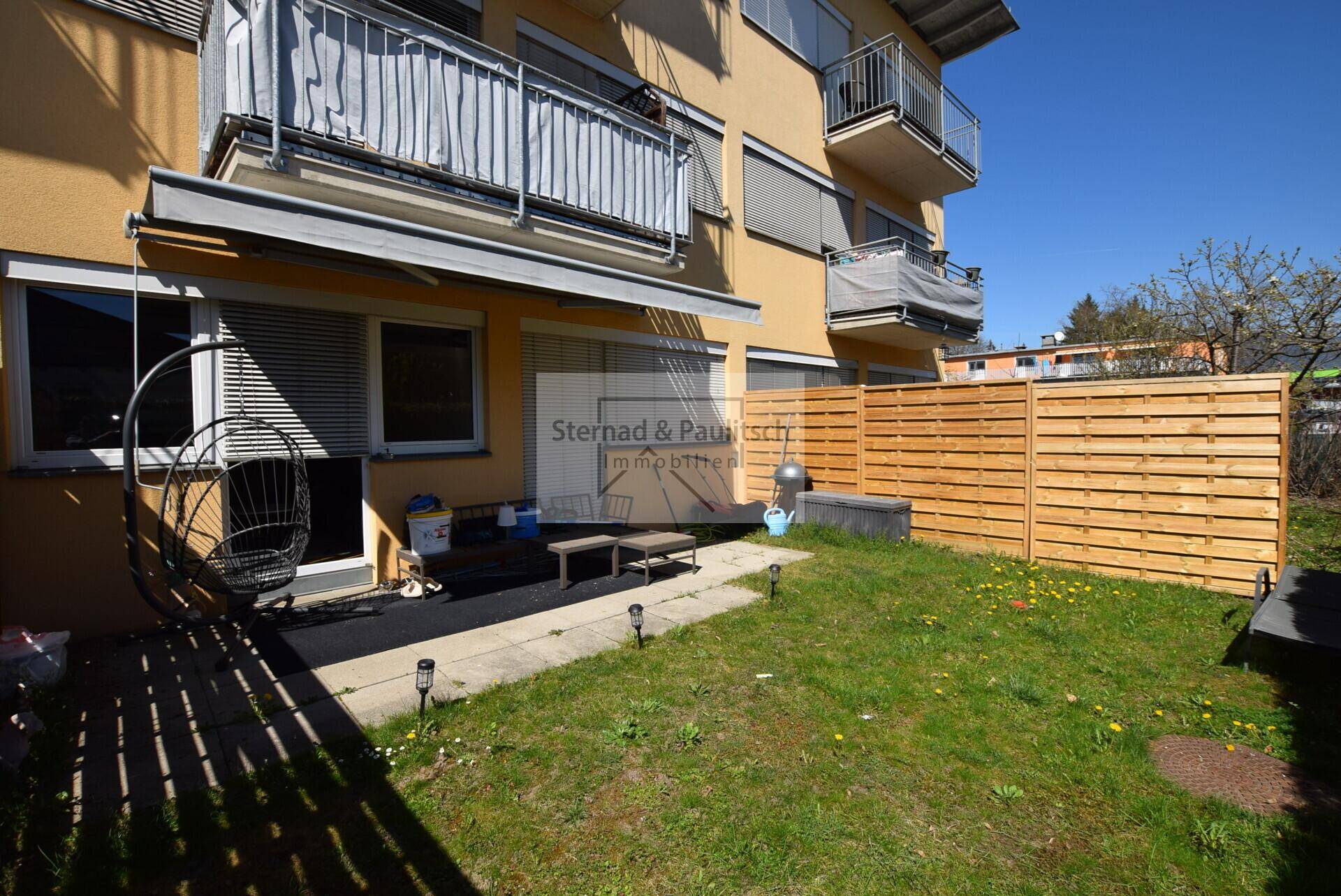 Unmöblierter Gartenbereich mit Terrasse und Holzzaun hinter dem Gebäude.