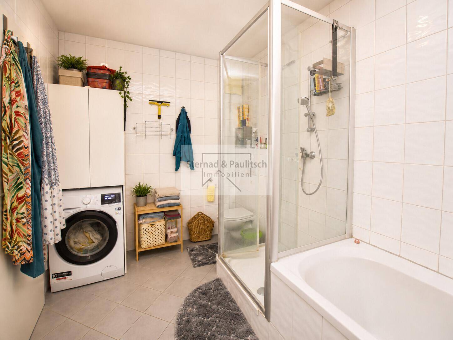 Modernes Badezimmer mit Badewanne, Duschkabine und Waschmaschine, hell gefliest und funktional.