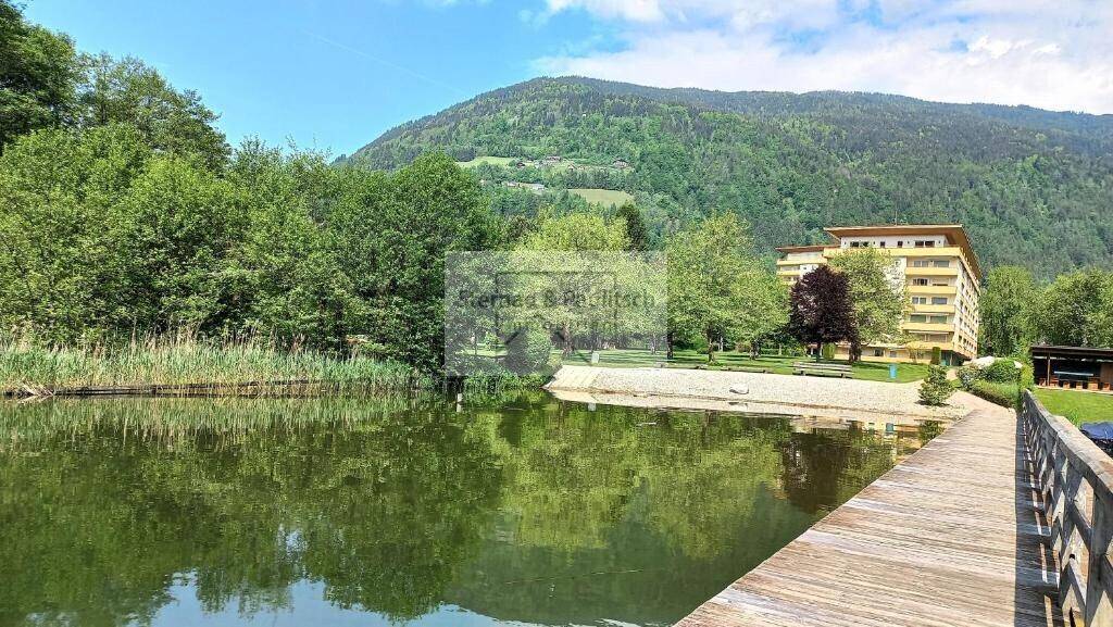 Idyllische Seenlandschaft mit bewaldeten Bergen und einem Gebäude am Ufer.